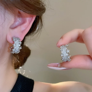Macro shot of silver C-shaped earrings with sparkling cubic zirconia on model