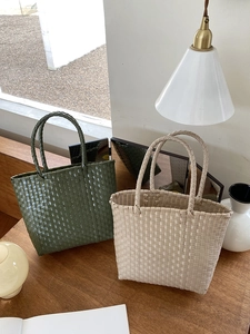 Detail of hand-woven straw tote bags in dark green and beige on a wooden tabletop