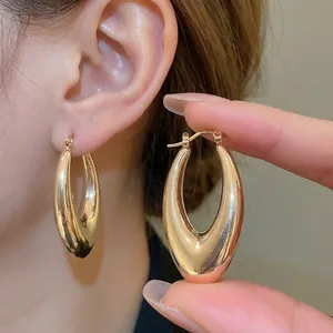 Minimalistische goldene Tropfenohrringe mit polierter Metallic-Oberfläche beim Tragen