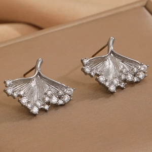 Detail of silver ginkgo leaf stud earrings with sparkling pavé-set zircons on soft fabric