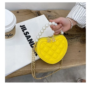 Detail of yellow heart-shaped girls bag with pearl handle and metal flower zipper