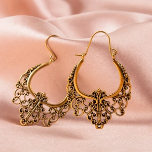 Detailed view of vintage hollow-out fan-shaped earrings on pink silk fabric background