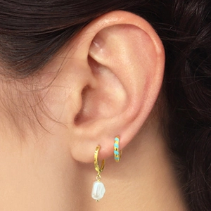 Detailed view of elegant pearl drop earrings and blue striped gold hoops on model ear