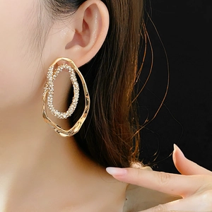 Close-up of gold-plated oval stud earrings with white zircons worn by a model