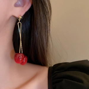 Close-up of elegant red cherry earrings with gold chains worn by a model