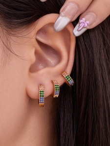 Close-up of gold huggie earrings with pink green and blue stones on ear