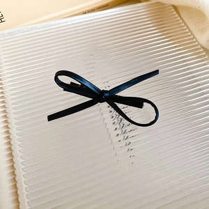 Detailed close-up of a black faux leather bow hair clip on a ribbed glass tray