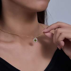 Macro shot of gold square pendant with olive green gemstone worn on model collarbone