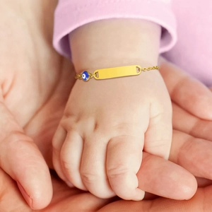 Close-up of baby evil eye gold bracelet with engravable bar on a soft background