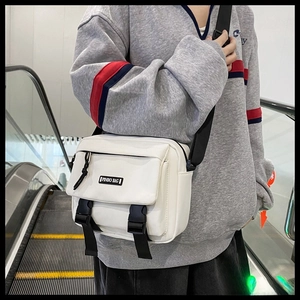 Close-up of white canvas crossbody bag with black nylon straps and twin buckle closure