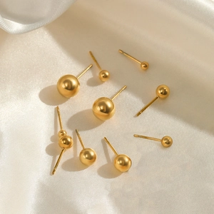 Minimalist gold ball stud earrings in various sizes on soft white silk fabric background