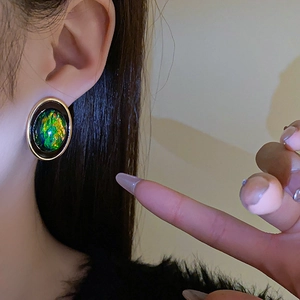 Gros plan d'une boucle d'oreille vintage ronde avec bord doré et pierre en résine verte
