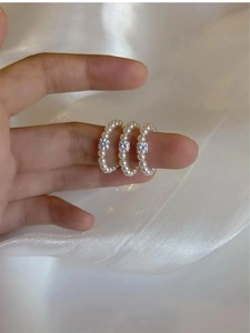 Close-up of triple-layered pearl rings with zircon on finger against white silk