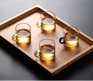 Set of four heat-resistant glass tea cups with colored handles on a wooden serving tray