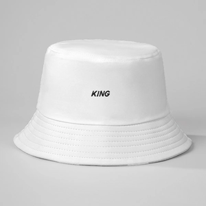 Detail of white cotton bucket hat with black KING embroidery on a soft gray background