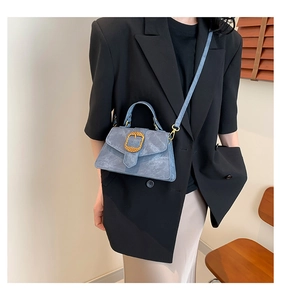 Detail of blue vintage textured crossbody bag with gold buckle on black blazer