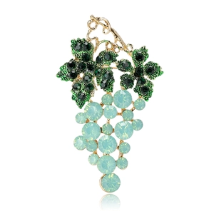 Elegant gold grape brooch with emerald green leaf and sky blue crystals on white background