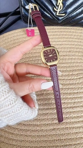 Macro shot of gold square watch with burgundy leather strap on a textured background