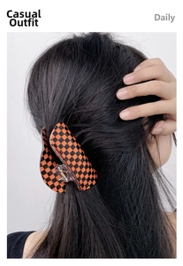 Detail of a large orange and black checkered acrylic hair claw clip for daily hairstyle