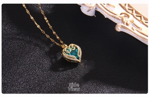 Macro side view of golden heart pendant with green crystal and intricate floral engraving