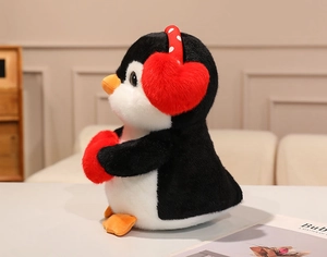 Side view of plush penguin doll with red heart earmuffs and heart pillow decoration