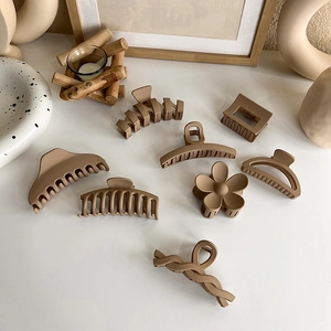 Close-up of matte milk tea brown hair claws in floral and geometric shapes on a wooden desk