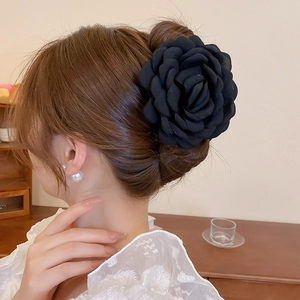 Elegant black fabric camellia flower hair clip accessory shown on a messy bun hairstyle
