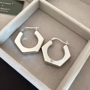 Macro shot of silver hexagon geometric hoop earrings on gray velvet jewelry display box