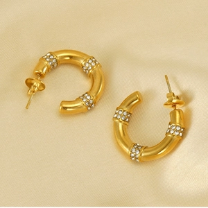 Macro detail of gold C-shape bamboo earrings with sparkling rhinestone inlay on silk