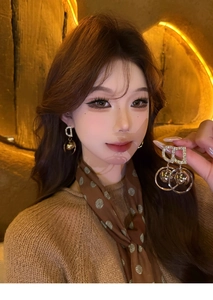 Close-up of golden CD letter earrings with a polished metal ball and sparkling rhinestones
