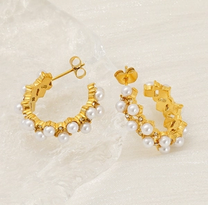 Detailed view of C-shaped gold pearl earrings with zircon accents on silk