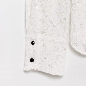 Close-up of white lace sleeve with contrasting black decorative buttons on the cuff