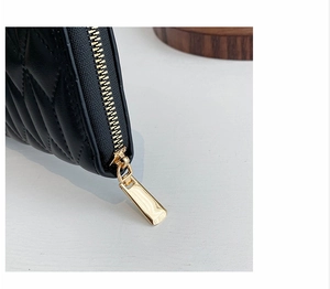 Detail shot of golden alloy zipper and black quilted leather on a long clutch wallet