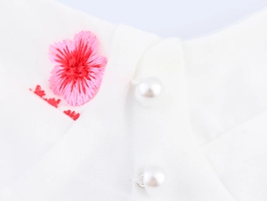 Détail de broderie florale rose et boutons de perles sur robe en maille blanche