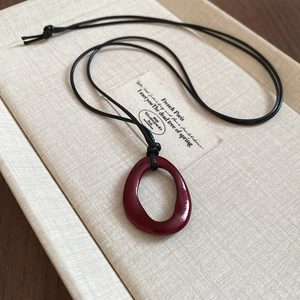 Détail d'un collier pendentif bordeaux géométrique irrégulier sur fond en lin beige
