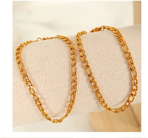 Detail of a shiny gold Figaro chain bracelet wrapped on a beige fabric jewelry stand