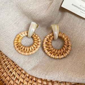 Detailed close-up of woven rattan pendant earrings with marble resin studs on linen fabric