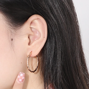 Detail view of rose gold twisted hoop earrings worn on a model for a chic look