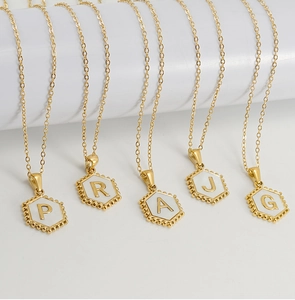 Macro view of five 18K gold hexagon initial necklaces with white enamel inlay