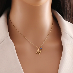 Détail d'un collier doré avec pendentif lettre M et une perle bleue mauvais œil