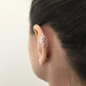 Detail view of a silver leaf-shaped ear cuff and stud earring on a model