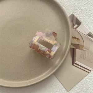 Dettaglio di una pinza per capelli quadrata marmorizzata rosa e ambra su vassoio ceramico