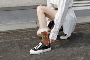Detail of white crew socks with orange and green face art worn with black sneakers
