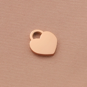 Close-up of polished rose gold heart charm pendant with bail on textured fabric