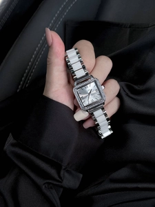 Close-up of square silver watch with crystal bezel and white ceramic linked bracelet