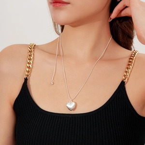 Gros plan d'un pendentif cœur en argent brossé sur une fine chaîne porté par un mannequin