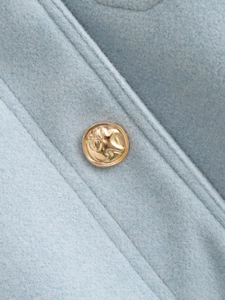 Detailed macro shot of light blue tweed fabric texture with an embossed gold metal button