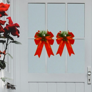 Pair of red Christmas ribbon bows with pine needles and cones on a white glass door