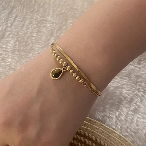 Detail of a double-layered gold bracelet with a brown tiger eye teardrop charm