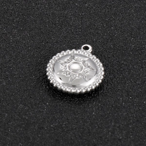 Detailed macro view of silver stainless steel round pendant with sun pattern and bead edge